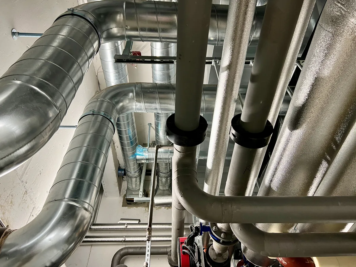 An der Decke sind mehrere Lüftungs- und Wasserrohre angebracht.